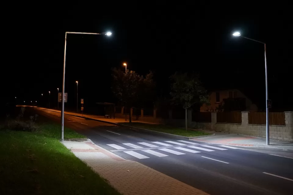 Empty street with crosswalk lit by two tall street lights at night.